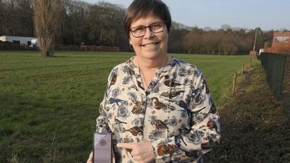 Dama stoji u polju i pokazuje na svoj Dexcom prijemnik